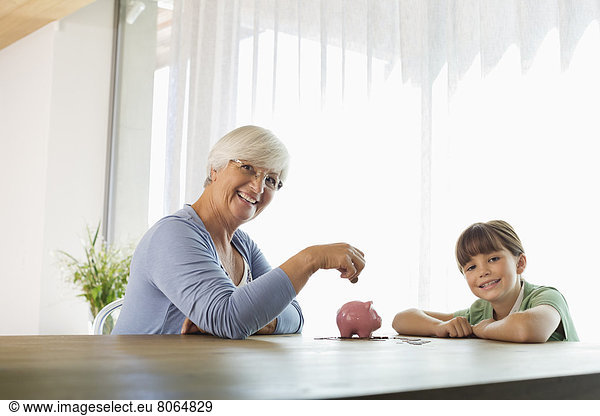 Older woman and granddaughter filling piggy bank
