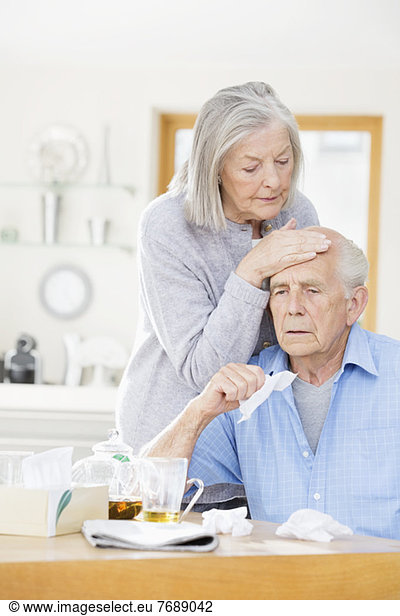 Older woman feeling sick husband's forehead