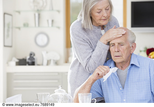 Older woman feeling sick husband's forehead