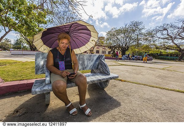 Older woman on her cell phone under an umbrella in Nueva Gerona on Isla de la Juventud  Cuba.