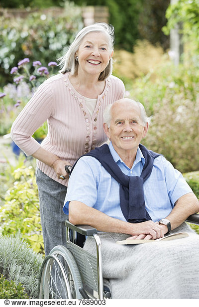 Older woman pushing husband's wheelchair outdoors