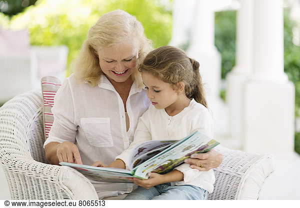 Older woman reading to granddaughter on porch