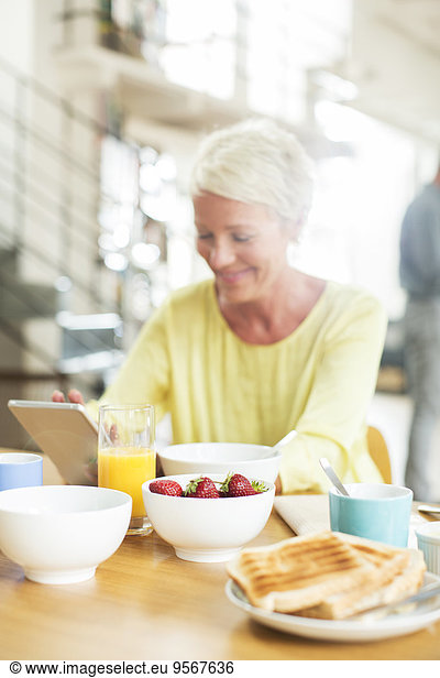 Older woman using digital tablet at breakfast table