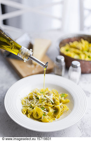Olive oil pouring into plate of Italian tortellini with grana cheese