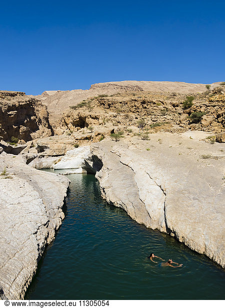 Oman,  Sharqiyah,  two people bathing at Wadi Bani Khalid