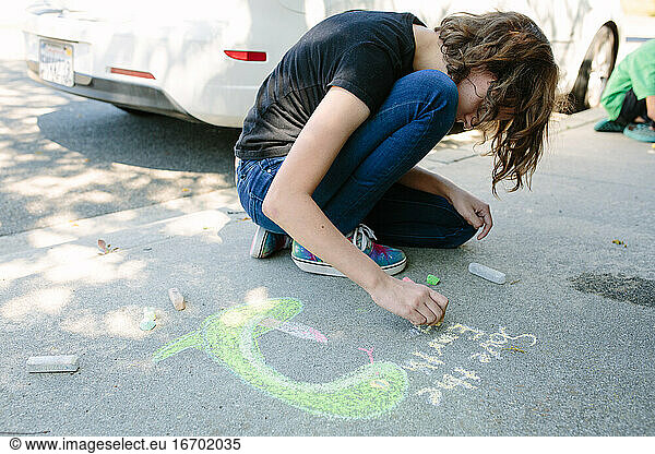 On Earth Day a teen girl draws on concrete with chalk