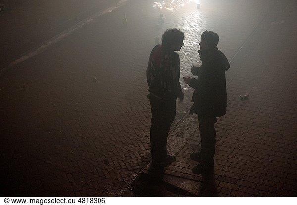 On newyearseve 2010/2011 two young men meet and talk outside in the street  while smoke from fireworks is drifting by.