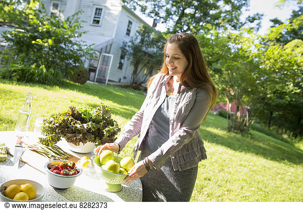On The Farm. A Woman In A Farmhouse Garden  Preparing A Table With Fresh Organic Foods  Fresh Vegetables And Salads And Bowls Of Fresh Fruit  For A Meal.