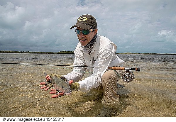 One fly fisherman holding Bonefish on the beach while is fishing in Los Roques National Park Venezuela.
