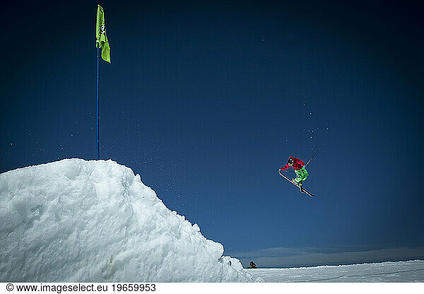 One male skier launching off of a jump at a ski resort.