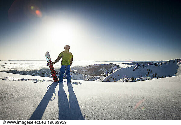 One male snowboarder silhouette looking over mountains and fresh snow.