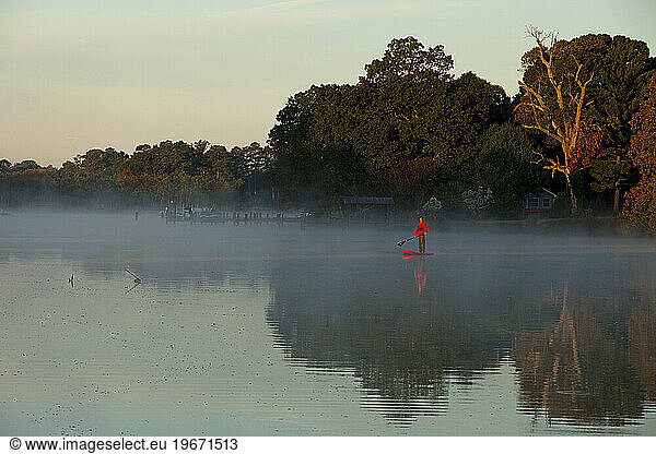 One man stand up paddleboarding (SUP) in fog and morning light.