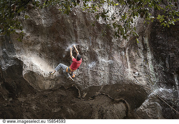 One man wearing red holds with both hands on rock wall while climbing