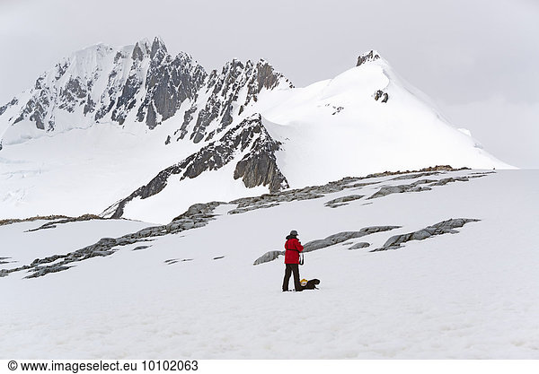 One person standing on the ice in front of a snow-covered mountain.