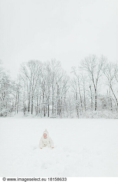One year old baby sits in a snowy field in Maryland in winter.