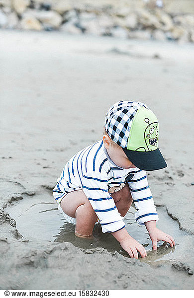 One year old boy playing in a puddle of water on the beach.
