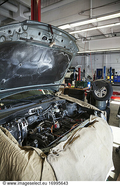 Open engine compartment of a car draped and ready for a mechanic in auto repair shop