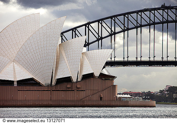 Opernhaus von Sydney bei Brücke gegen bewölkten Himmel
