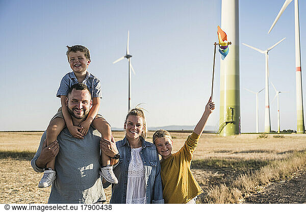 Optimistic family standing in wind park daughter carrying colorful pinwheel