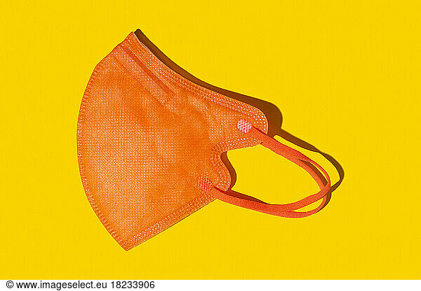 Orange colored FFP2 mask lying against yellow background