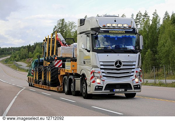 ORIVESI  FINLAND - AUGUST 27  2018: Mercedes-Benz Actros semi trailer of Hansedrive transports forest machinery on highway in Finland on overcast day.