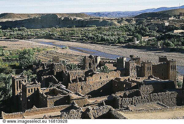 Ouarzazate Marokko Afrika - Blick von oben auf die alte Lehmarchitektur und die Lehmziegelgebäude der historischen Festung Ksar von Ait Benhaddou einer UNESCO-Weltkulturerbestätte an der ehemaligen Karawanenstraße zwischen der Sahara und Marrakesch. Die Anlage diente bereits als Drehort für zahlreiche Filmproduktionen von Lawrence von Arabien über James Bond bis hin zu Game of Thrones. Im Hintergrund ist das enge Flusstal der Asif Mellah zu sehen.