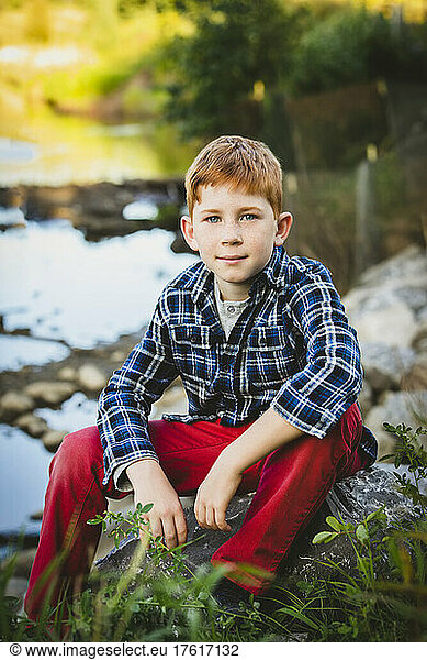 Outdoor portrait of a boy with red hair sitting beside a creek; Edmonton  Alberta  Canada