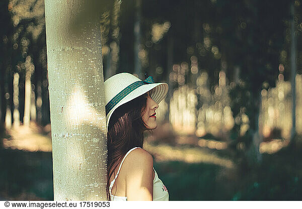 Outdoor portrait of a young woman enjoying her time in nature wearing a hat and white flowery dress