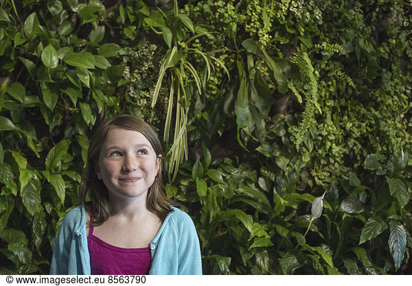 Outdoors in the city in spring. An urban lifestyle. A young girl standing in front of a wall covered with ferns and climbing plants.