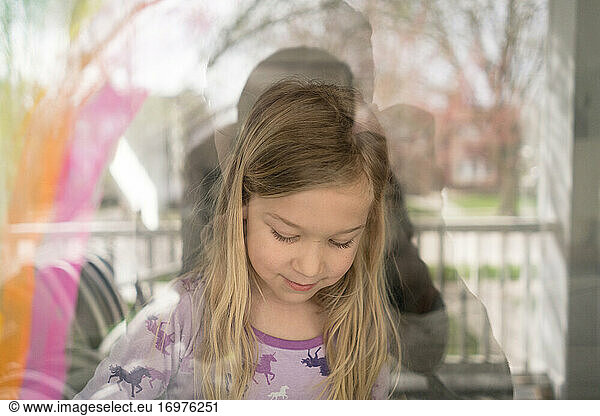 outside in view of blond girl painting rainbow on window