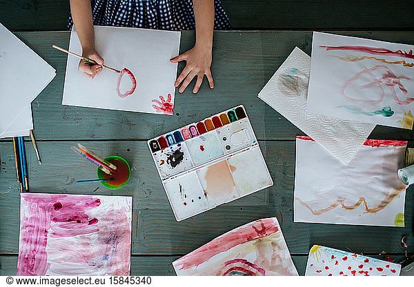 over head view of young girl painting bright pictures on table