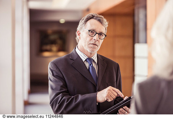 Over shoulder view of businessman using digital tablet in office corridor