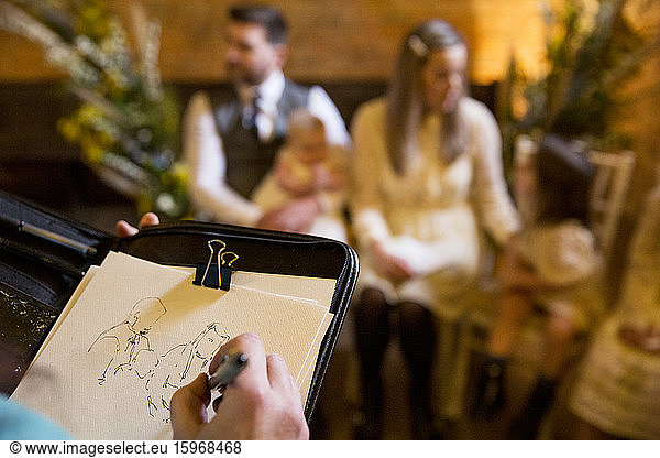 Over the shoulder view of artist sketching family during naming ceremony in an historic barn.