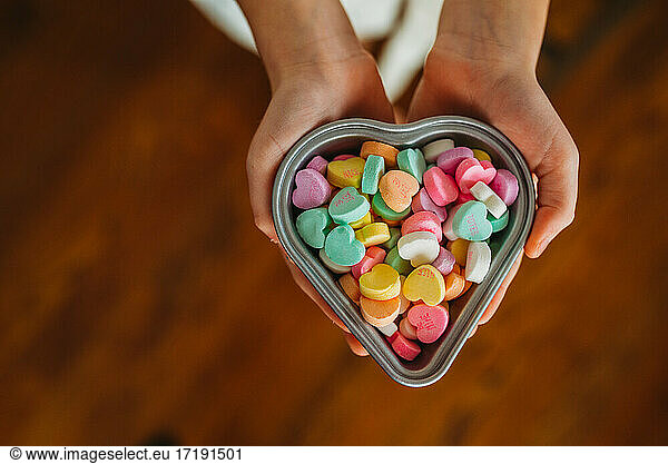 overhead of child's hands holding candy hearts in heart dish