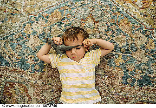 overhead of toddler laying on carpet with a dinosaur covering face