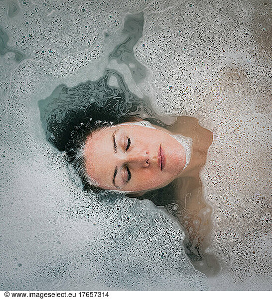 Overhead of woman relaxing in a bubble bath with eyes closed.