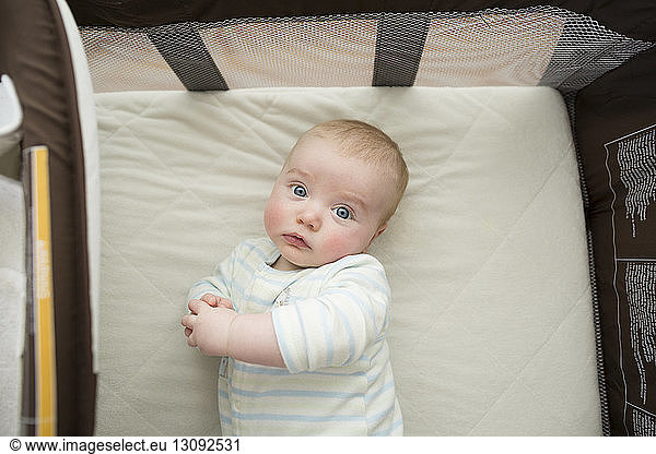 Overhead portrait of cute baby boy lying on mattress in pack n' play at home