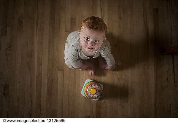 Overhead portrait of cute baby boy with toy sitting on floor at home