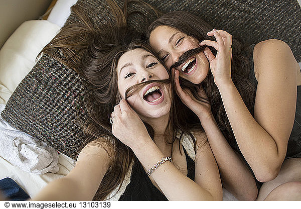 Overhead portrait of female friends making artificial mustache with hair
