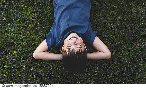Overhead shot of boy laying on grass with arms behind head laughing.