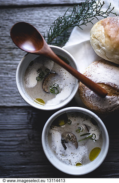 Overhead shot of mushroom soup with spoon and buns on wooden table