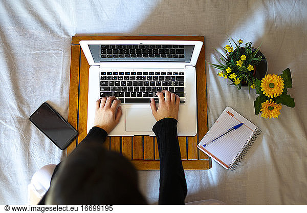 Overhead view of a woman working in bed with the computer.