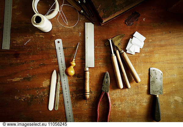 Overhead view of a workbench with hand tools for bookbinding.
