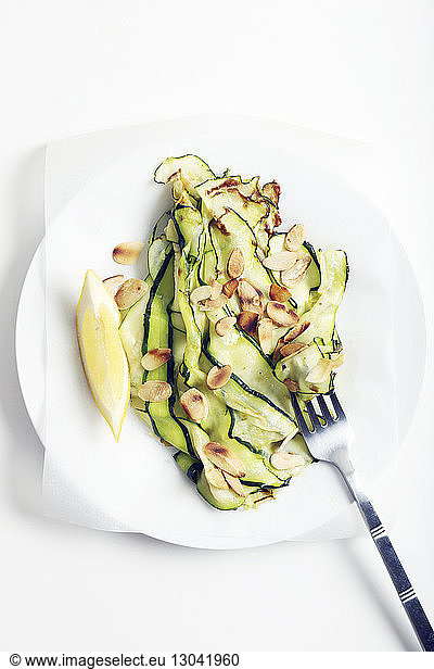 Overhead view of avocado slices with nuts and lemon served in plate over white background
