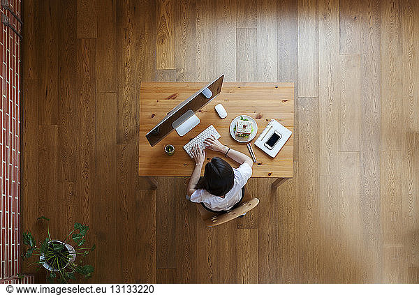 Overhead view of businesswoman using desktop computer at table on hardwood floor in home