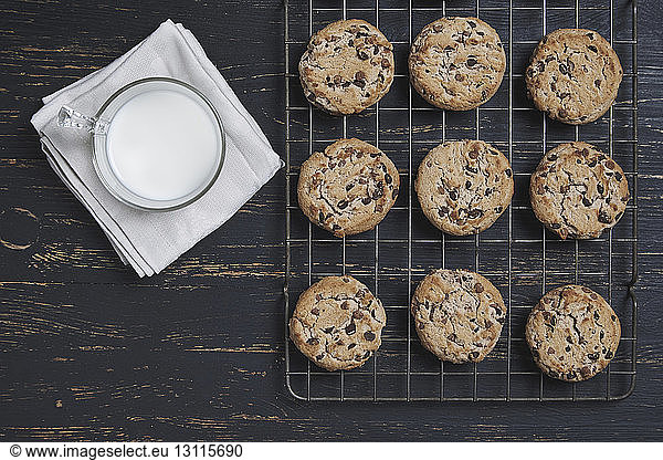 Overhead view of chocolate chip cookies on cooking rack with milk over wooden table