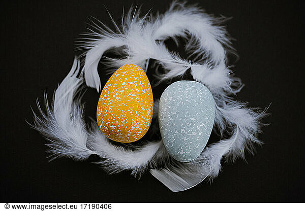 Overhead view of colored Easter eggs and feathers on black background