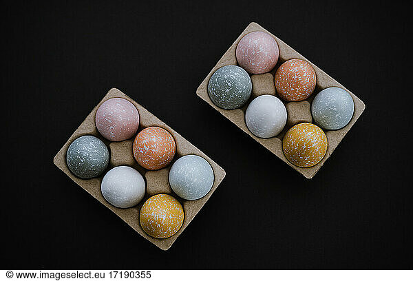 Overhead view of colorful Easter eggs in egg carton on black
