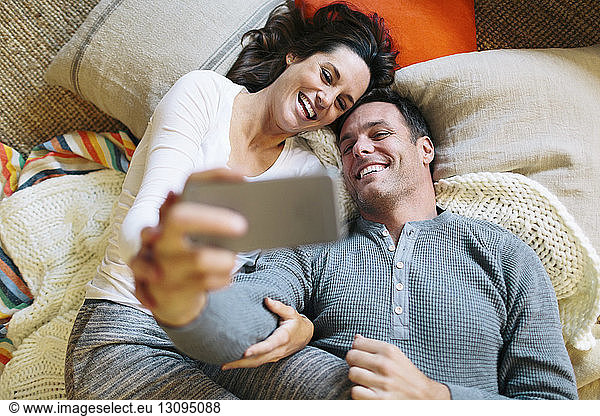 Overhead view of couple taking selfie while lying on carpet at home