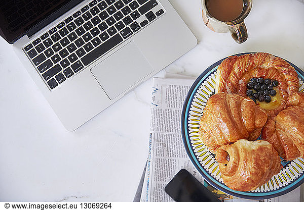 Overhead view of croissants in plate by laptop computer on table